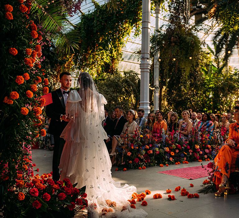 Orange and red wedding floral arch with pink rug lining the aisle with colourful wedding flowers at botanical wedding 