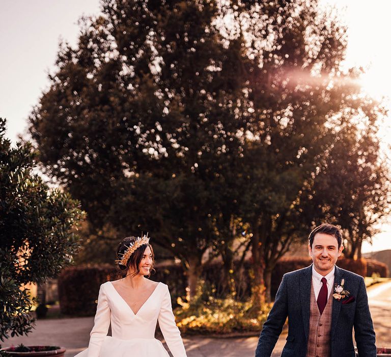 Groom in navy suit walking hand in hand with their son in a brown suit and bride in princess wedding dress and crown 