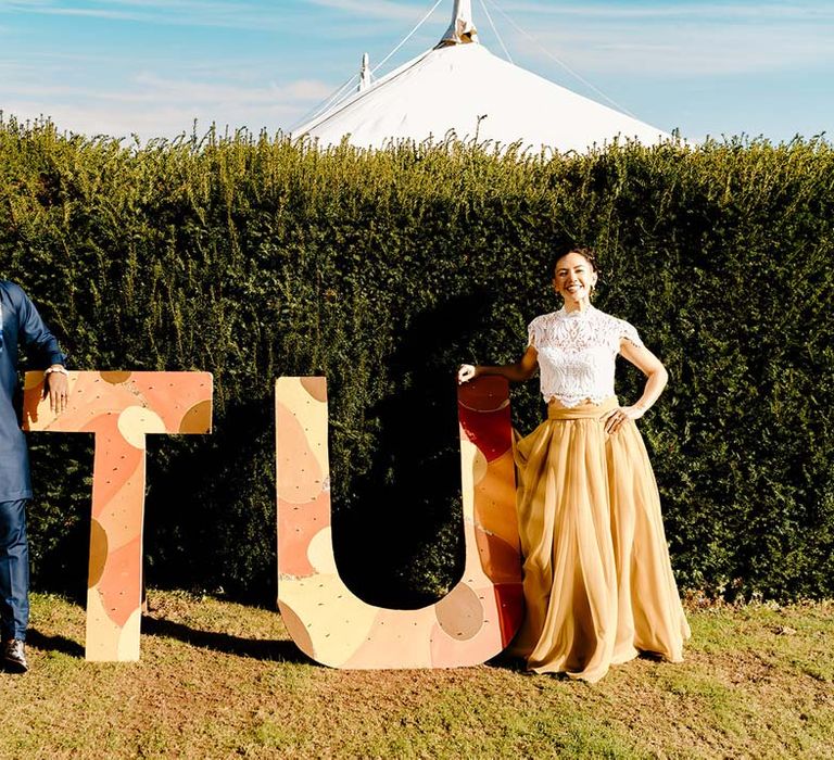 Bride in white mesh lace bridal crop top and yellow wedding skirt standing by large wedding decorations with groom in traditional Nigerian wedding outfit