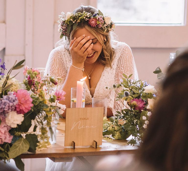 Bride in delicate lace gown with pastel wedding flower crown reacts to the wedding speeches 