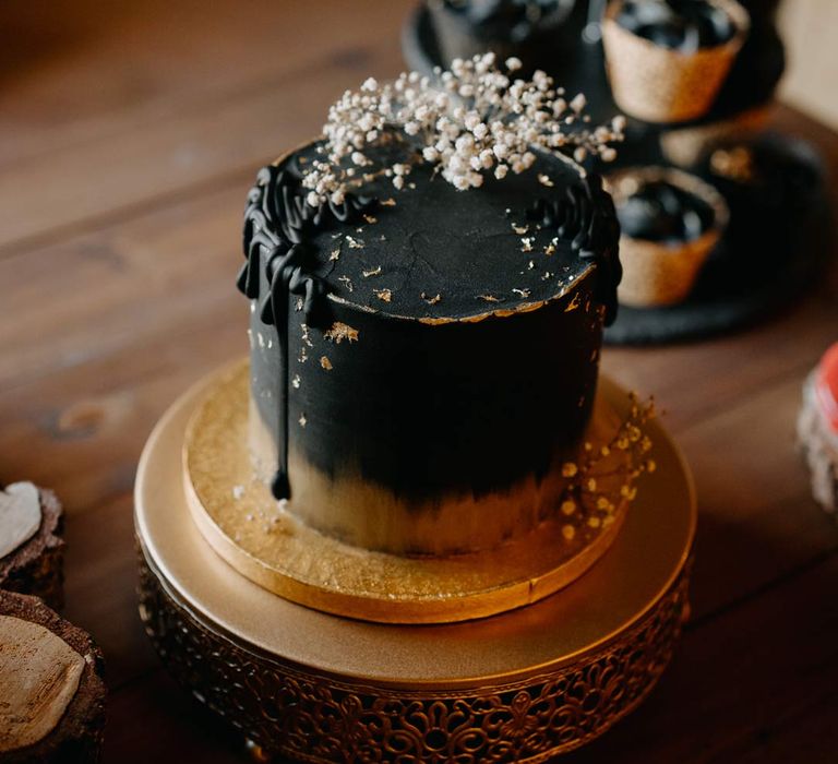 Single black wedding cake with gold rim and dried flower wedding cake toppers on gold cake stand