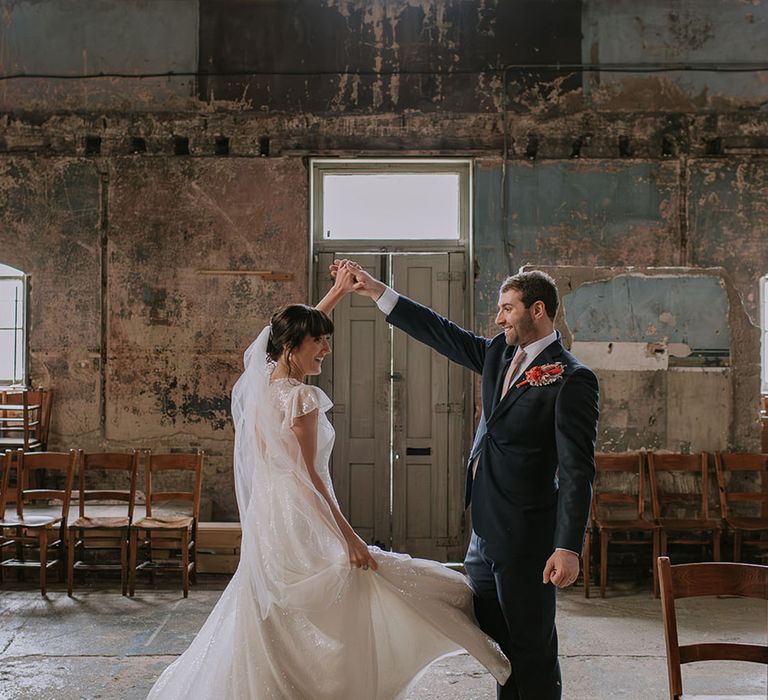 Groom in navy suit spins the bride in a sparkly wedding dress around for couple portrait 