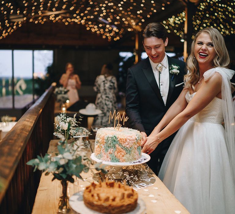 Colourful pastel rug wedding cake being cut by the bride and groom 