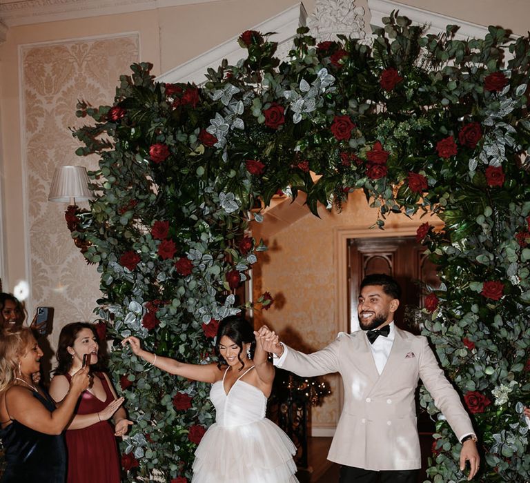 Red rose flower arch with the bride in reception dress and groom in beige tuxedo for the reception 