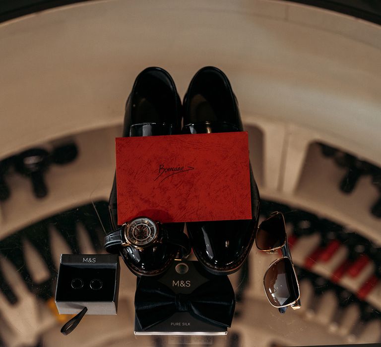 Flatlay of groom accessories including wedding shoes, watch, wedding cufflinks, and sunglasses