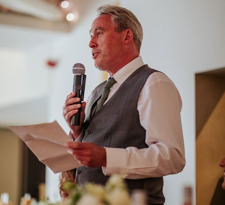 Father of the bride in a grey waistcoat stands to make his wedding speech 