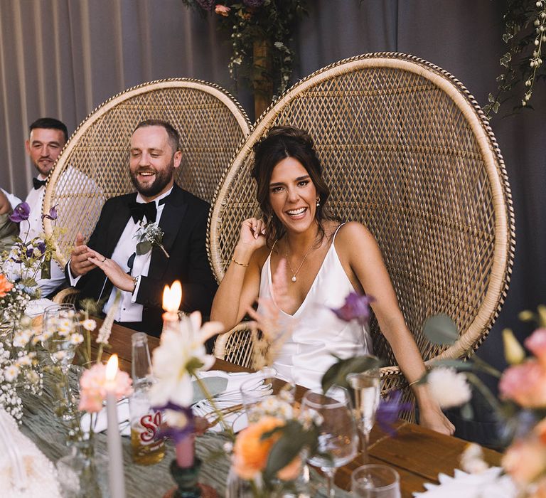 The bride and groom is on peacock chairs at their wedding breakfast on the top table 