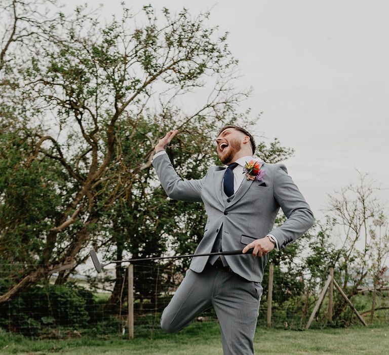 Mini golf game played by groom in grey wedding suit for relaxed and laid back wedding 