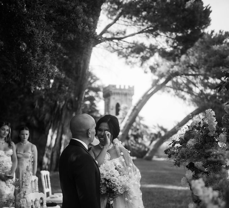 Groom in tuxedo and bride in embellished wedding dress at the altar of outdoor wedding 