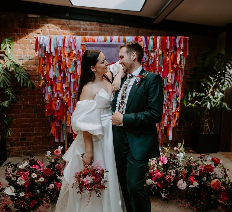 Bride and groom posing in front of their colourful altar decorations with streamers 