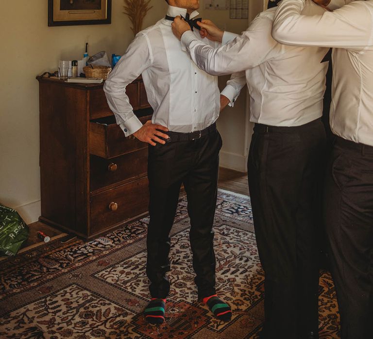 The groom and groomsmen help each other put on their black bow ties 