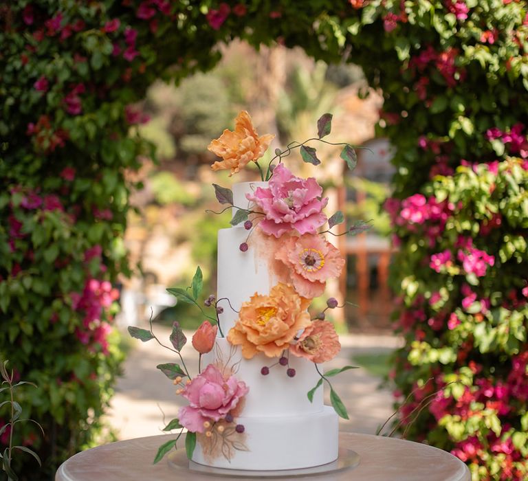 White iced tiered wedding cake decorated with colourful pink and orange wedding flowers 