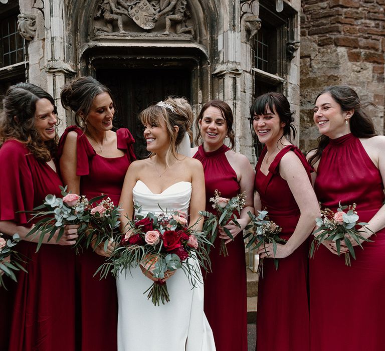 Bridal party wearing red burgundy mismatched bridesmaid dresses posing with the bride 