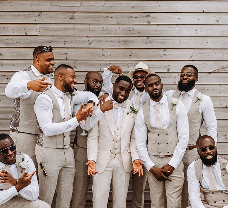 Groomsmen wearing beige waistcoats and trousers posing with groom for group photo 