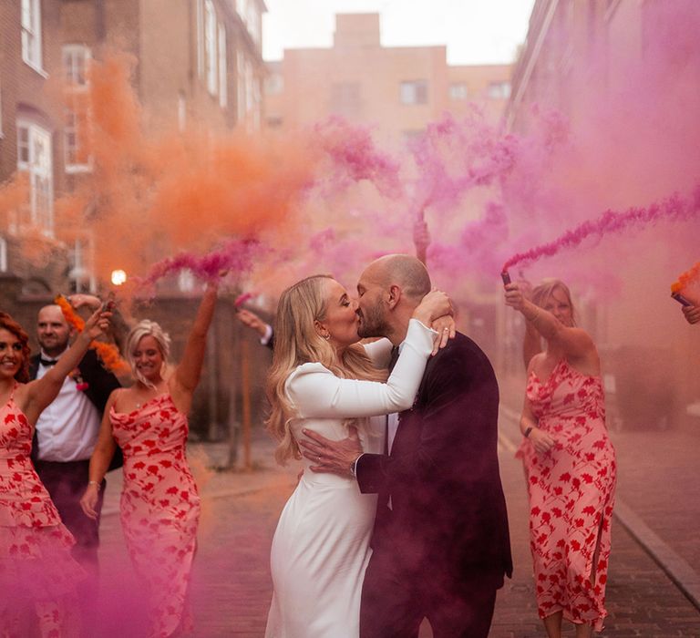 Bride and groom share intimate kiss surrounded by pink and orange smoke for couple portrait