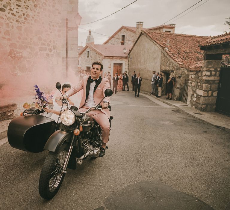 bride and groom on a motorcycle waving a pink smoke bomb