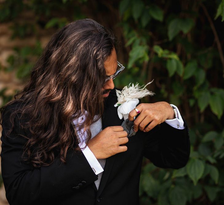 Groom in black suit putting on his white rose buttonhole 