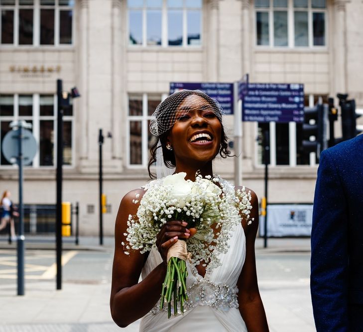 Bride in birdcage veil smiling holding her rose and gypsophila bouquet 