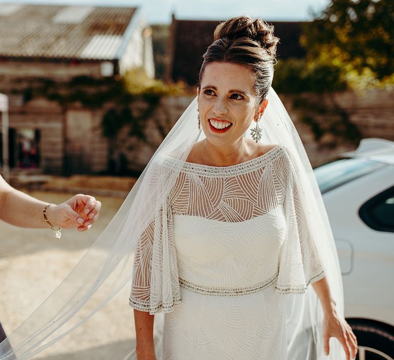 Bride wearing red lipstick with veil being carried