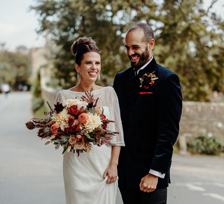 Bride & groom stand together outdoors carrying floral bouquet 