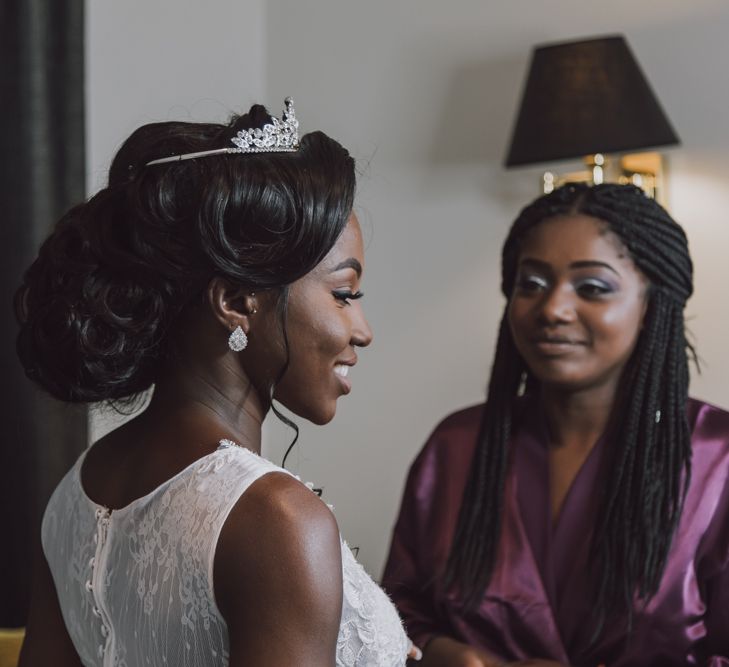 A bride smiles getting ready. She has a low bun in her hair and wears a tiara.