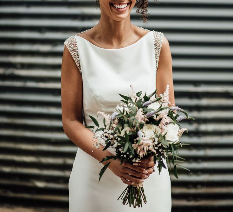 A Black bride wears all her curly hair loose and up high on her head. She laughs at the camera whilst holding her bouquet.