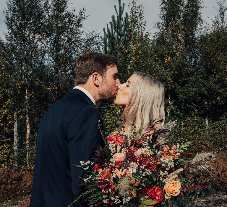 Bride & groom kiss in Scottish countryside whilst she holds floral bouquet 