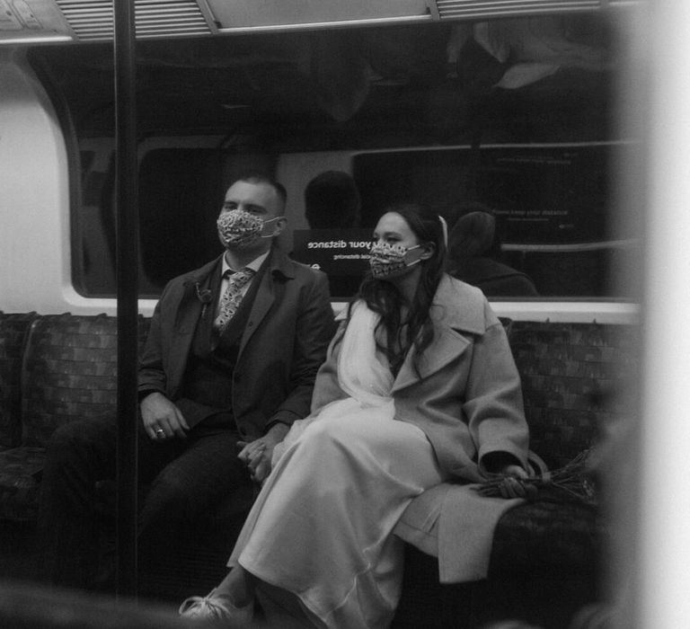 Bride and groom sat on London underground tube wearing masks for city elopement 