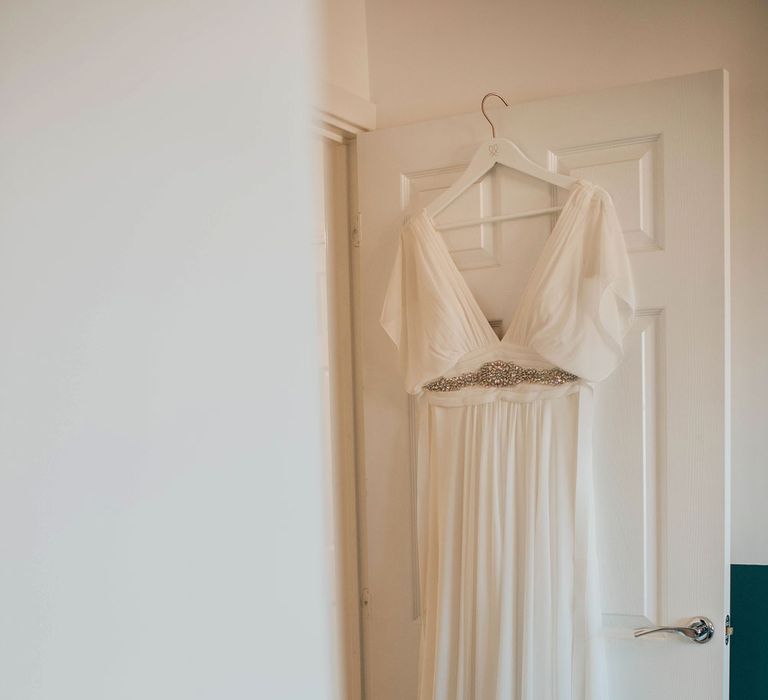 White boho wedding dress with silver gem detailing hanging on bedroom door