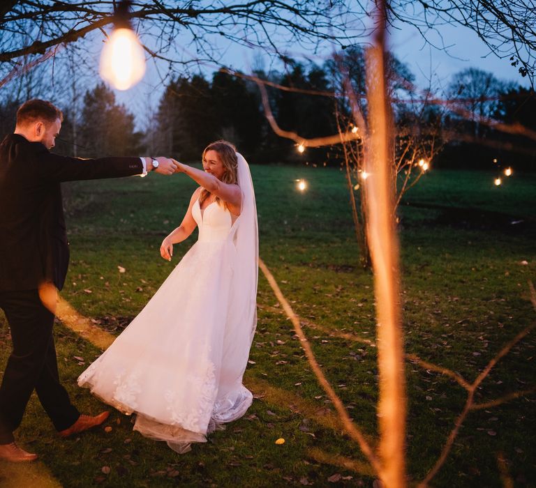 Bride & groom dance together outdoors surrounded by lights