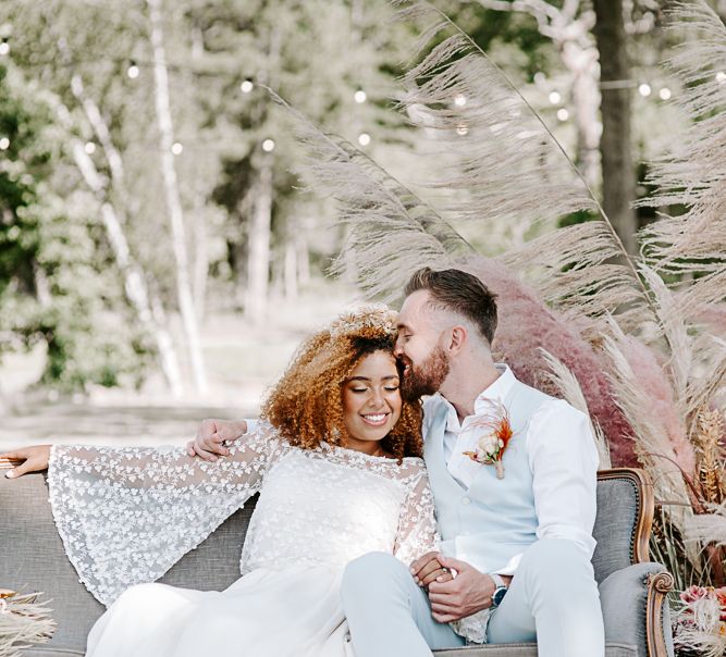 Bride & groom embrace whilst sat down on grey sofa 