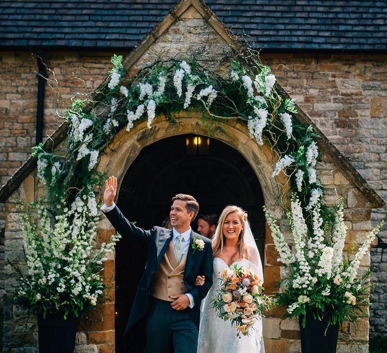 Bride and groom outside church wedding with white flower arch around the church entrance 