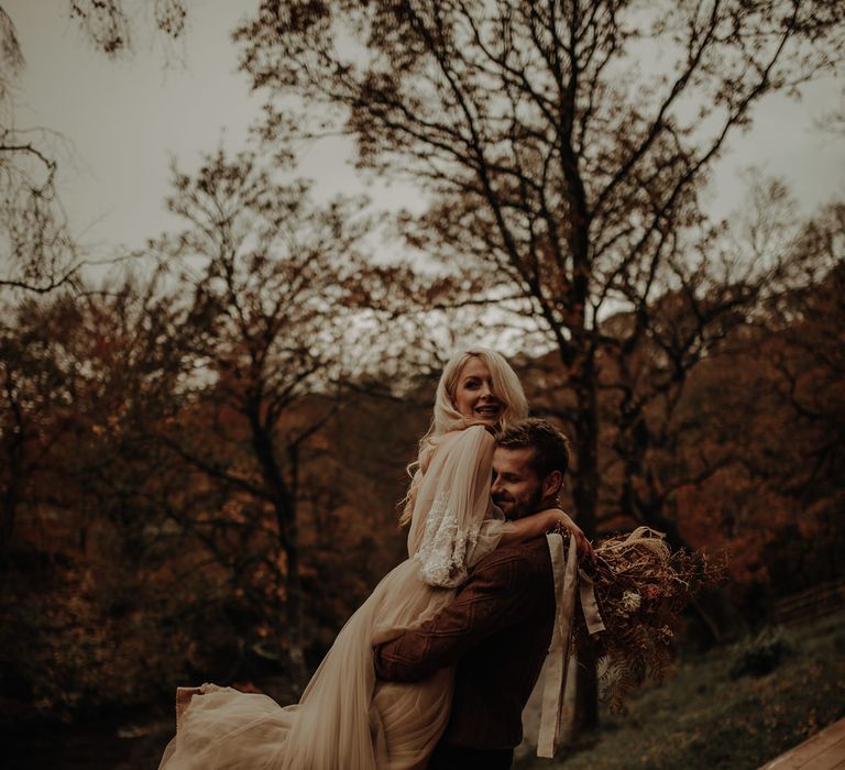 Bride in a layered tulle wedding dress with beaded sleeve detail being picked up by her groom in a jumper 