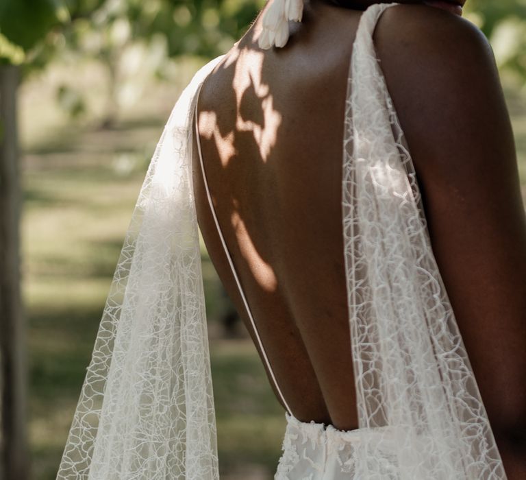 A Black bride with cropped hair looks back over her shoulder to the camera. Her dress has a watteau train. 