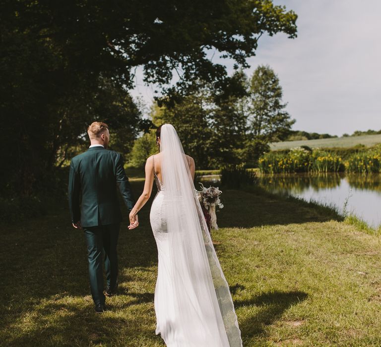 Bride & groom walk together through countryside on the day of their wedding 