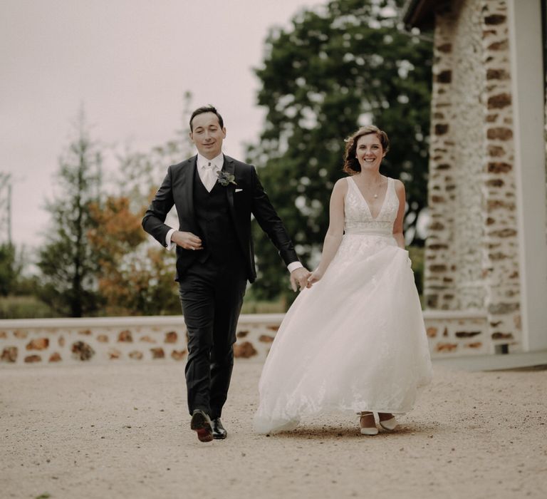 The bride and groom walk hand in hand outside La Ferme d'Armenon