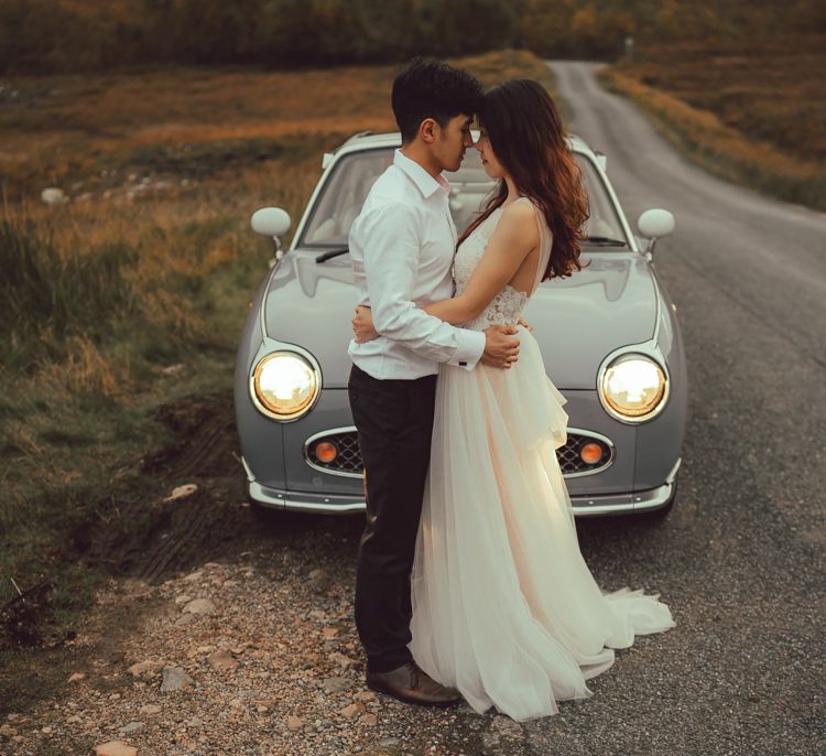 Couple stand in front of vintage car and embrace