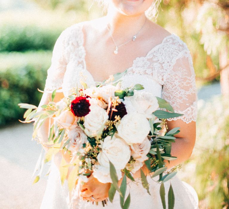 The bride holding her bouquet of red dahlias, white roses and olive leaves