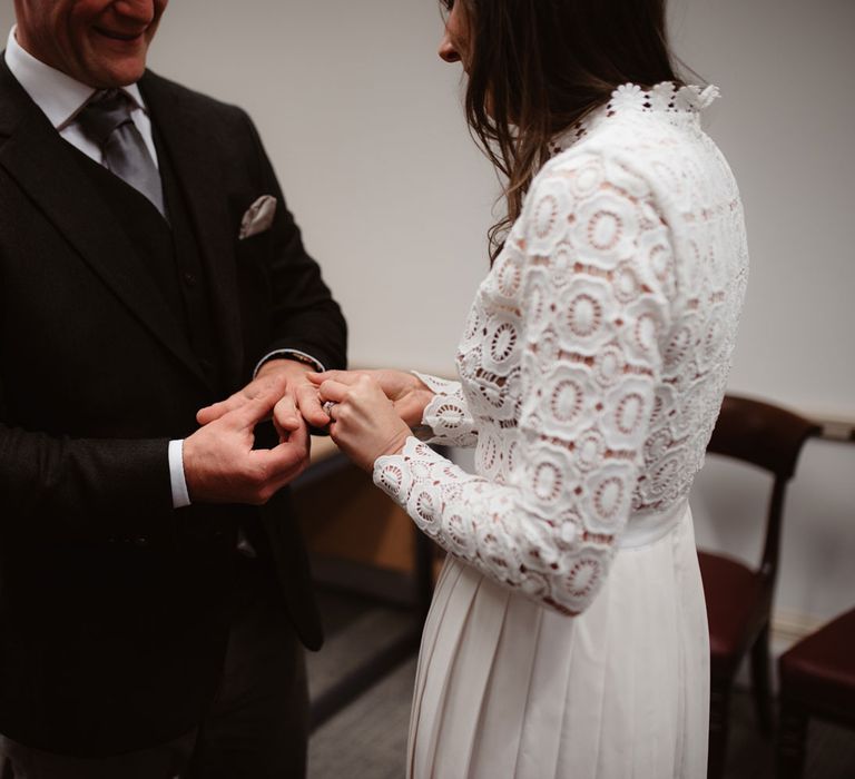 Groom in brown woollen suit and bride in Self Portrait wedding dress exchange rings inside Bristol Registry Office