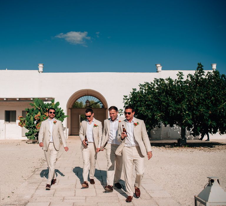 The groomsmen wearing beige linen suits with an orange lapel flower