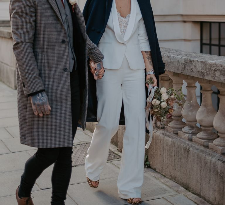 Bride and groom both in suits and coats look at each other and smile while walking