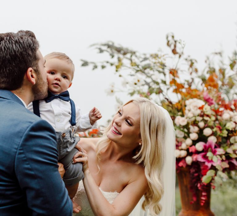 The bride and groom lift up their 7 month old son, giving him a kiss and celebrating their wedding day