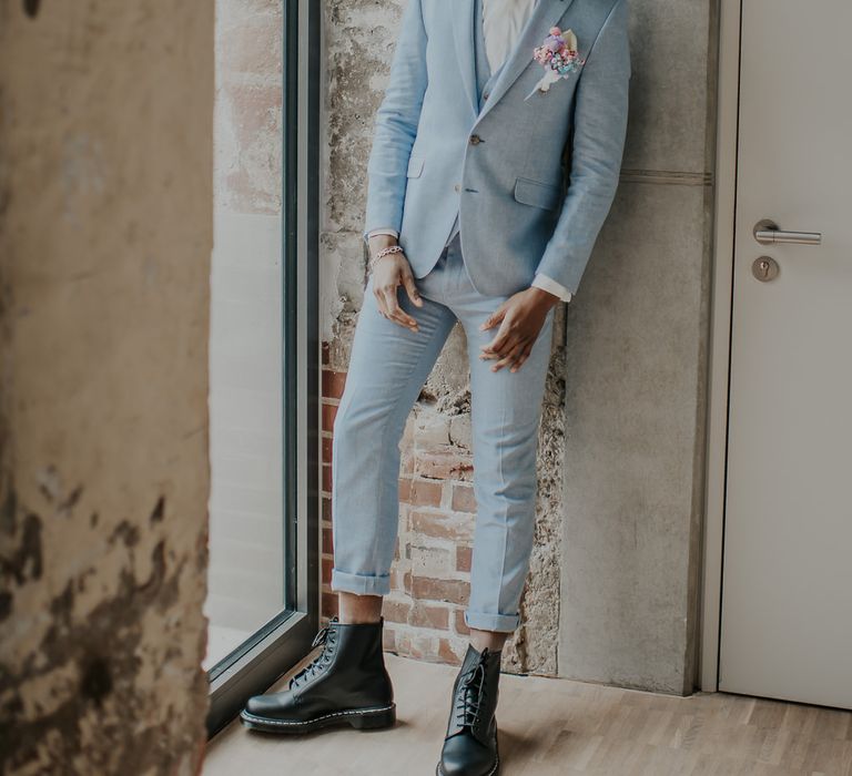 Stylish groom in a pale blue wedding suit with black hat and metal bow tie 