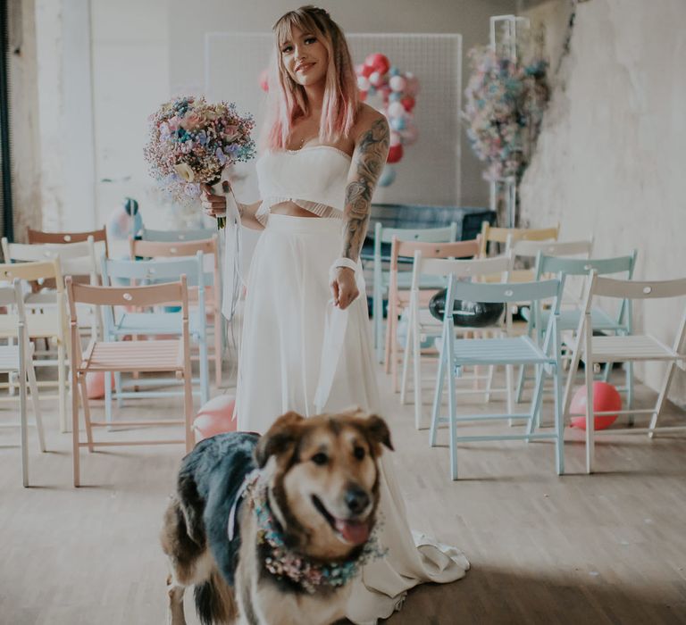 Bride in separates holding a pastel gypsophila bouquet and the lead for her dog with a flower collar 