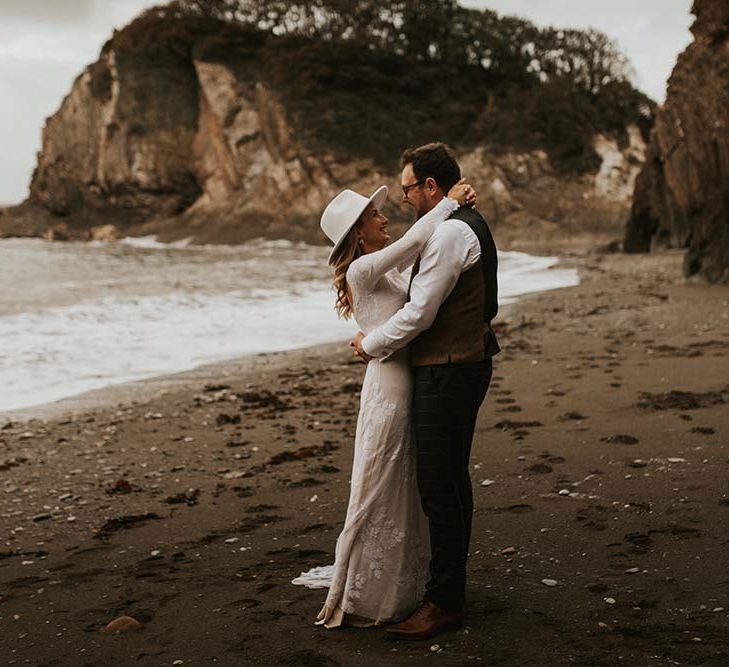 Bride in a long sleeve appliqué wedding dress kissing her groom on the beach in Devon at their intimate seaside elopement 