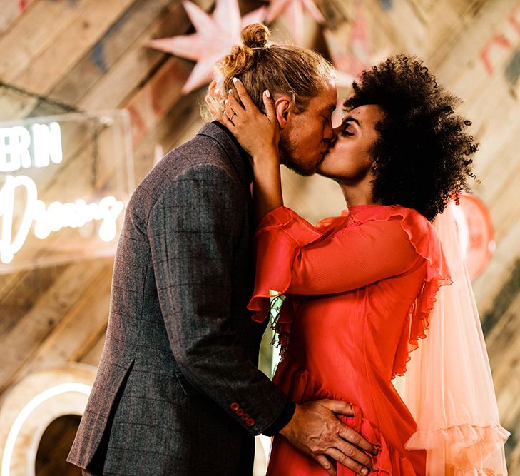 Bride and groom kissing in front of a neon sign decorated wall 