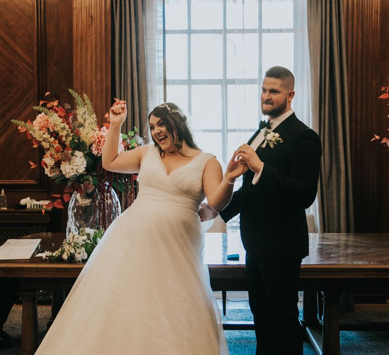 Bride celebrates after wedding ceremony as groom holds her hand and smiles