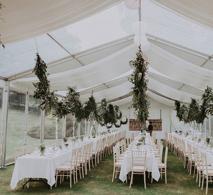 White marquee setting complete with three rows of tables and hanging floral installations for classic English wedding