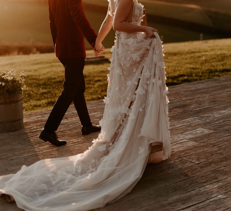 Golden hour portrait with bride in a lace appliqué wedding dress and groom in a red velvet tuxedo jacket 