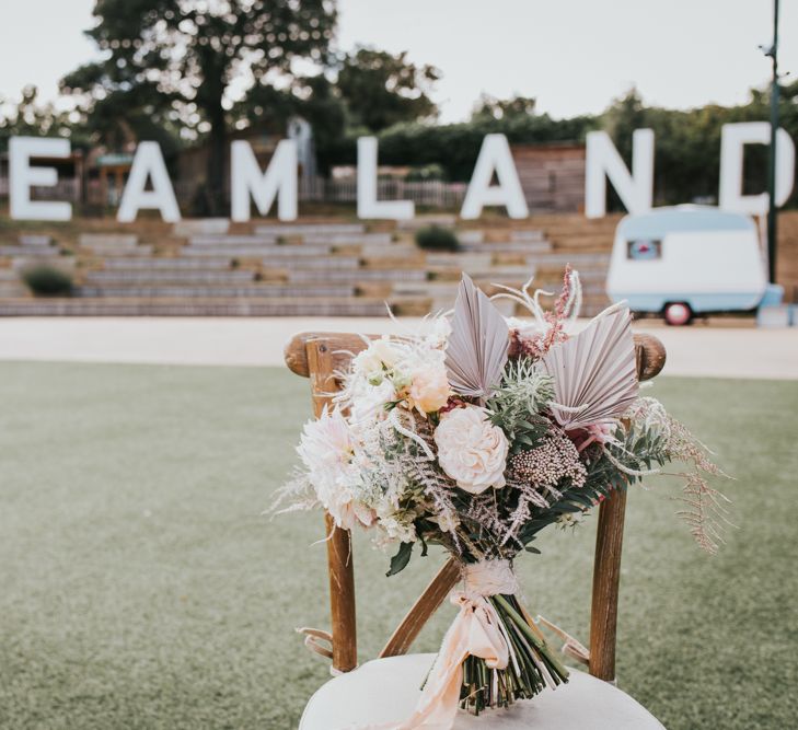 Pastel pink flower and dried palm leaves wedding bouquet resting on a chair with the giant Dreamland sign in the background 